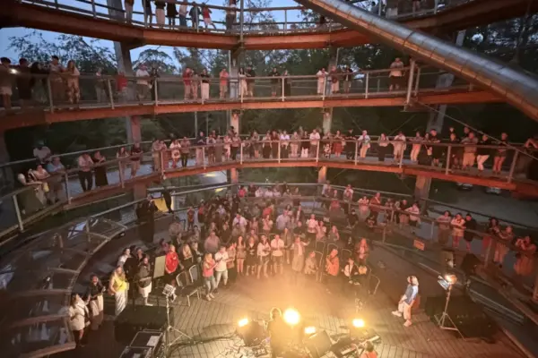 paddy casey_1800 1_1x A crowd gathers on multiple levels of a circular wooden structure, watching a live music performance illuminated by stage lights in the centre at dusk.